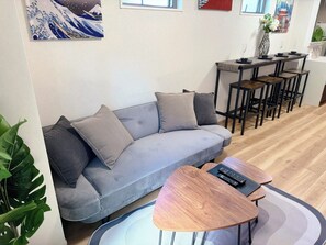 Een moderne woonkamer met een grijze bank, een houten salontafel, en een eethoek met een houten tafel en stoelen.