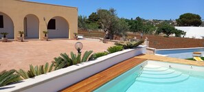 A pool area with a wooden deck, a white building with arches, and a view of a hillside with trees. - Apartment 'Appartamento Cosimo' with Sea View, Wi-Fi and Air Conditioning (Marina di Pescoluse)