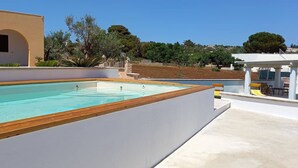 A swimming pool with a wooden deck, a white building with arches, and a view of a hilly landscape. - Apartment 'Appartamento Cosimo' with Sea View, Wi-Fi and Air Conditioning (Marina di Pescoluse)