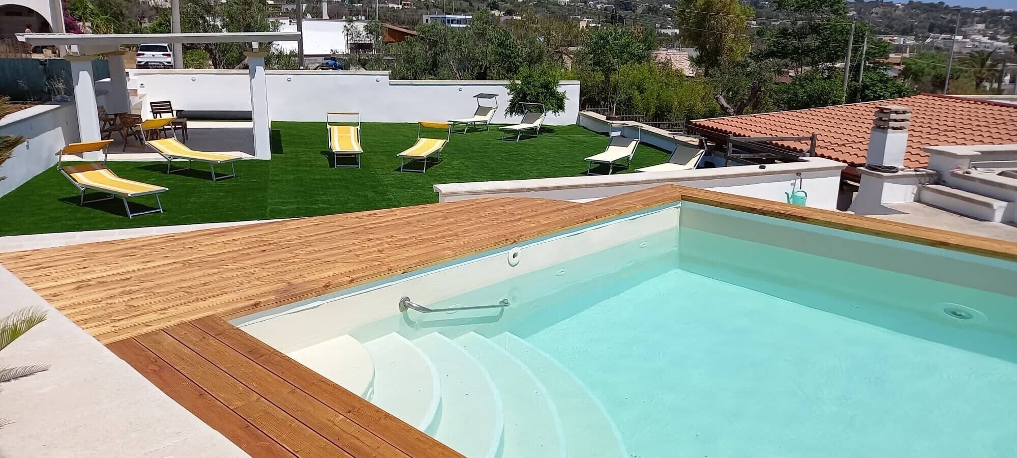 Una piscina en la azotea con terraza de madera y sillones de descanso.