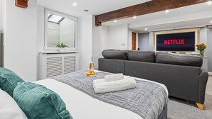 Ein modernes Schlafzimmer mit Bett, grauem Sofa und einem Fernseher, der 'NETFLIX' zeigt.