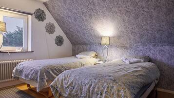 A bedroom with two beds, a radiator, a lamp, and a window with a view of trees.