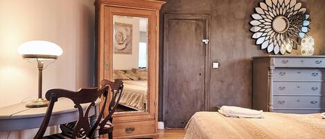 A bedroom with a wooden dresser, a mirror, a lamp, and a bed with a patterned bedspread.