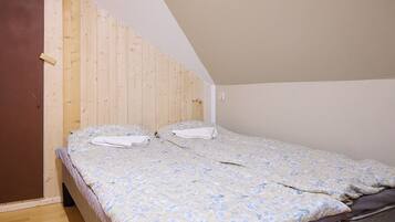Uma cama de solteiro com colcha floral num quarto com paredes de madeira e teto inclinado.