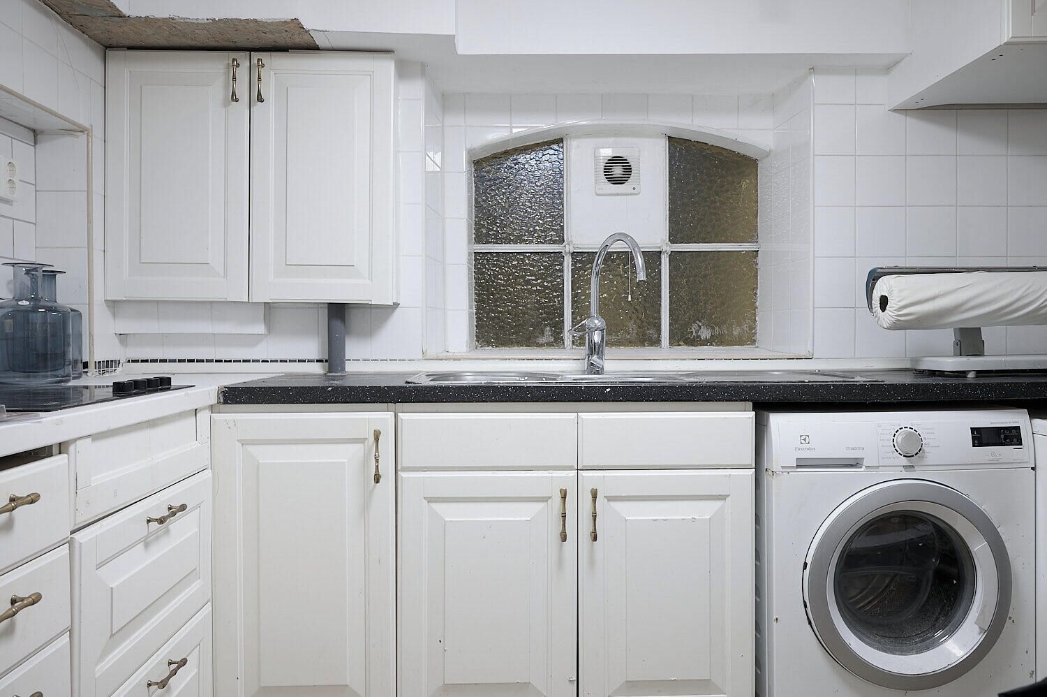 A kitchen with white cabinets, a stainless steel sink, a washing machine, and a window with a decorative glass panel.
