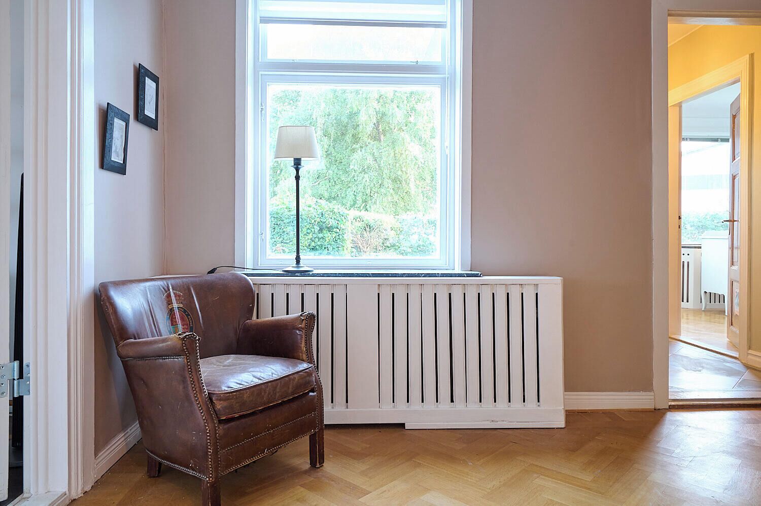 A room with a radiator, a brown leather chair, and a window with a view of greenery.