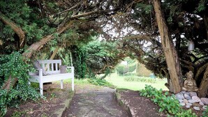 A stone pathway leading to a white bench surrounded by lush greenery and a Buddha statue. - Spacious six-bedroom home.  Söderrasens National Park is only 23 miles away. (helsingborg)