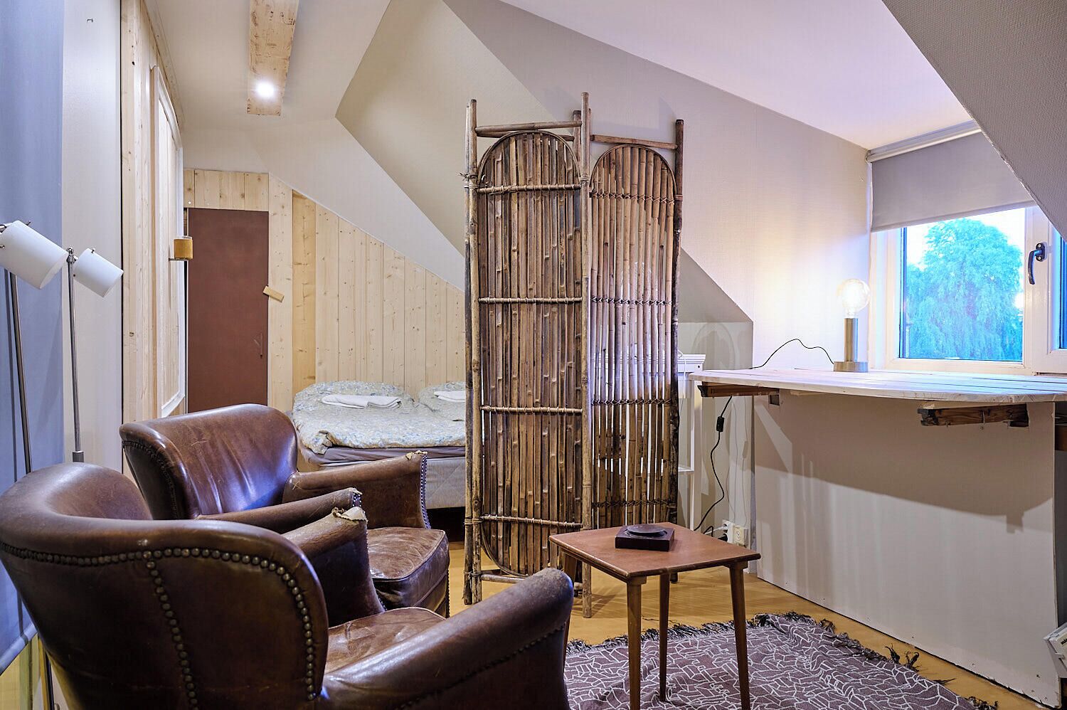 A room with a loft bed, a wooden chair, a small table, and a bamboo screen.