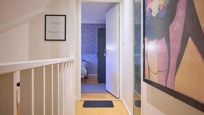 A narrow hallway with a wooden floor, a door leading to a bedroom with patterned wallpaper, and a framed inspirational quote on the wall. - Spacious six-bedroom home.  Söderrasens National Park is only 23 miles away. (helsingborg)