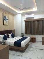 A modern hotel room with a large bed, a ceiling fan, an air conditioning unit, a small round table, and a chair.