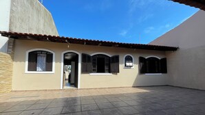 A building with a tiled patio, multiple windows with shutters, and a clear blue sky.