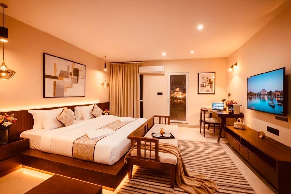 Habitación de hotel moderna con una cama grande, un escritorio con computadora, televisión y balcón con vista a la ciudad.