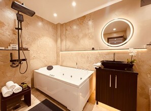A modern bathroom with a freestanding bathtub, a handheld showerhead, a round mirror with a light, and a dark wooden cabinet. - Hotel Hemsa Connect Udaipur (Udaipur)