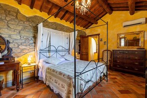 Une chambre à coucher avec un lit à baldaquin, des murs en pierre, des poutres en bois, une commode et un miroir.