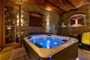 Une pièce aux murs de pierre, dotée d’un jacuzzi, de meubles en bois et d’une porte en verre.