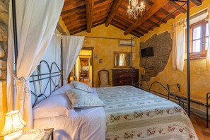 Une chambre à coucher avec un lit, des rideaux, un lustre, un mur en pierre, un plafond en bois et un miroir.