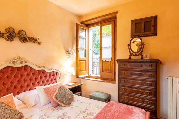 Una camera da letto con una testiera trapuntata, una cassettiera in legno, uno specchio e una finestra con tende.
