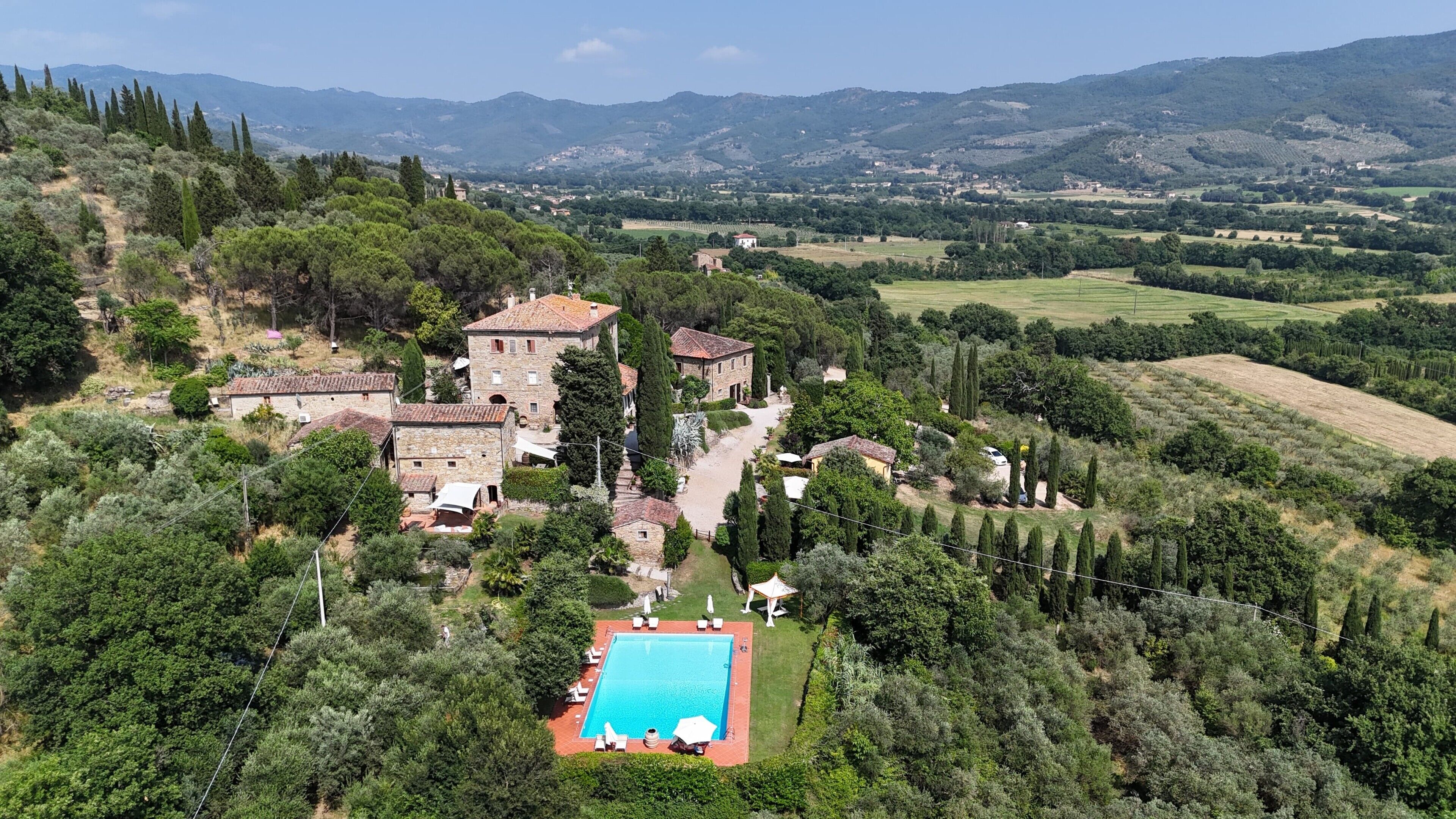 Eine Villa mit Schwimmbad, umgeben von üppiger Vegetation und Bergen im Hintergrund.