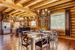 A log cabin interior with a dining area, kitchen, and large windows. - Legend Crest Lodge – Upscale Mountain Retreat w/ Indoor Pool, Views & Games! (Sevierville)
