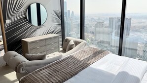 Un dormitorio con una cama grande, un espejo redondo, un aparador moderno y vistas a un paisaje urbano a través de ventanas amplias.