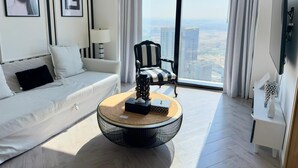 Una sala de estar moderna con un sofá blanco, un sillón a rayas, una mesa de centro redonda y un amplio ventanal con vistas a la ciudad.
