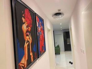 A hallway with two framed abstract paintings, a modern chandelier, and a green armchair in the background. - 3As Properties (Accra)