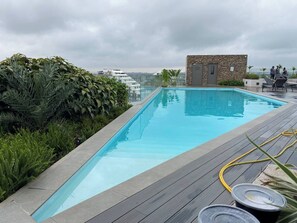 A rooftop pool with a wooden deck, surrounded by lush greenery and a stone building. - 3As Properties (Accra)