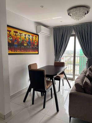A modern living room with a dining area, a large painting on the wall, and a view through the window. - 3As Properties (Accra)