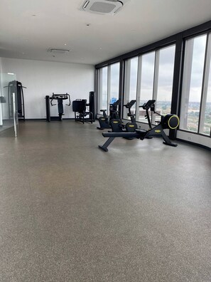 Et rummeligt fitnessrum med forskellig træningsudstyr, store vinduer og et højt til loftet.