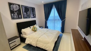 A bedroom with a bed, a nightstand, a TV, and a window with curtains. - 3As Properties (Accra)