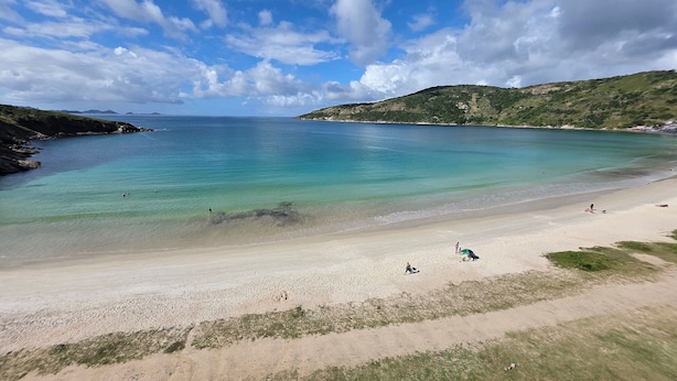 Ein Strand mit klarem Wasser, einem sandigen Ufer und Hügeln in der Ferne.