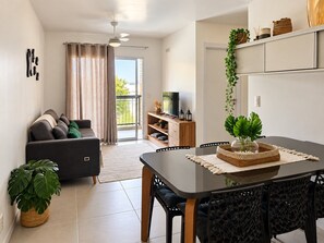 A modern living room with a sofa, a dining table, and a TV. - Apartamento Acessível em Cond. de Luxo  (Arraial do Cabo)