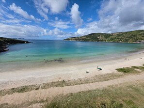 A beach with clear water, a sandy shore, and distant hills. - Apartamento Acessível em Cond. de Luxo  (Arraial do Cabo)