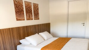 Quarto de hotel com duas camas, cabeceira de madeira, roupa de cama branca e três obras de arte nas paredes.