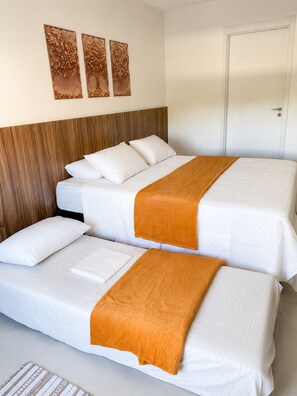 A hotel room with two beds, a wooden headboard, white bedding, and three wall art pieces. - Apartamento Acessível em Cond. de Luxo  (Arraial do Cabo)