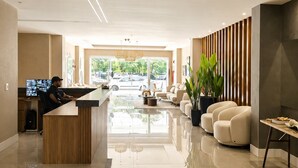 Um lobby moderno com balcão de recepção, área de estar e uma janela grande com vista para carros estacionados.