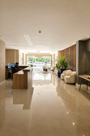 A modern lobby with a reception desk, seating area, and a large window with a view of parked cars. - Apartamento Acessível em Cond. de Luxo  (Arraial do Cabo)