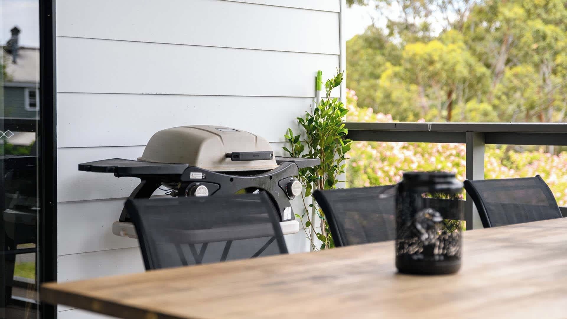 Een terras met een barbecue, stoelen en een tafel.