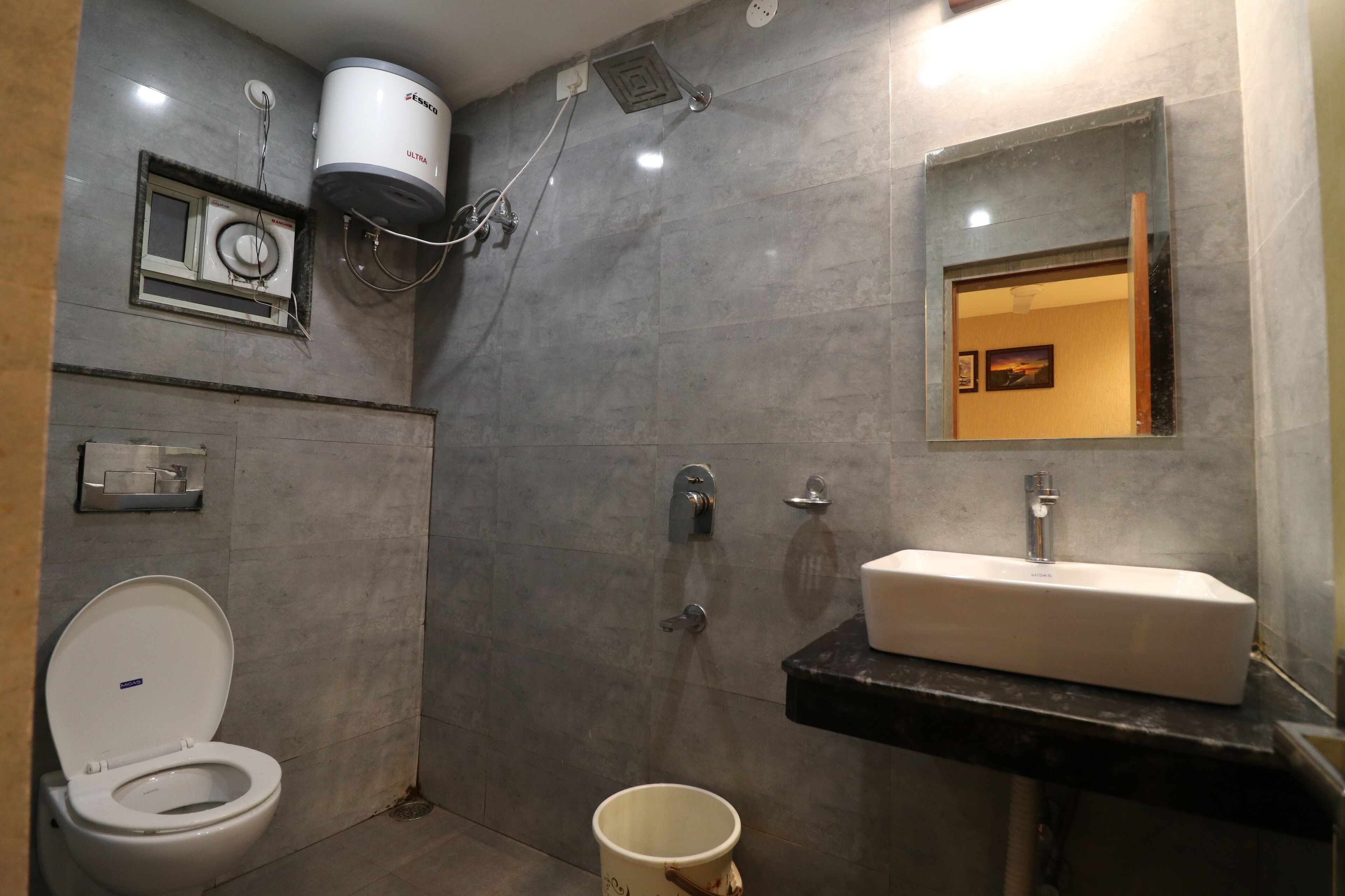 A bathroom with a white toilet, a sink with a mirror, and a shower with a ceiling-mounted water heater.