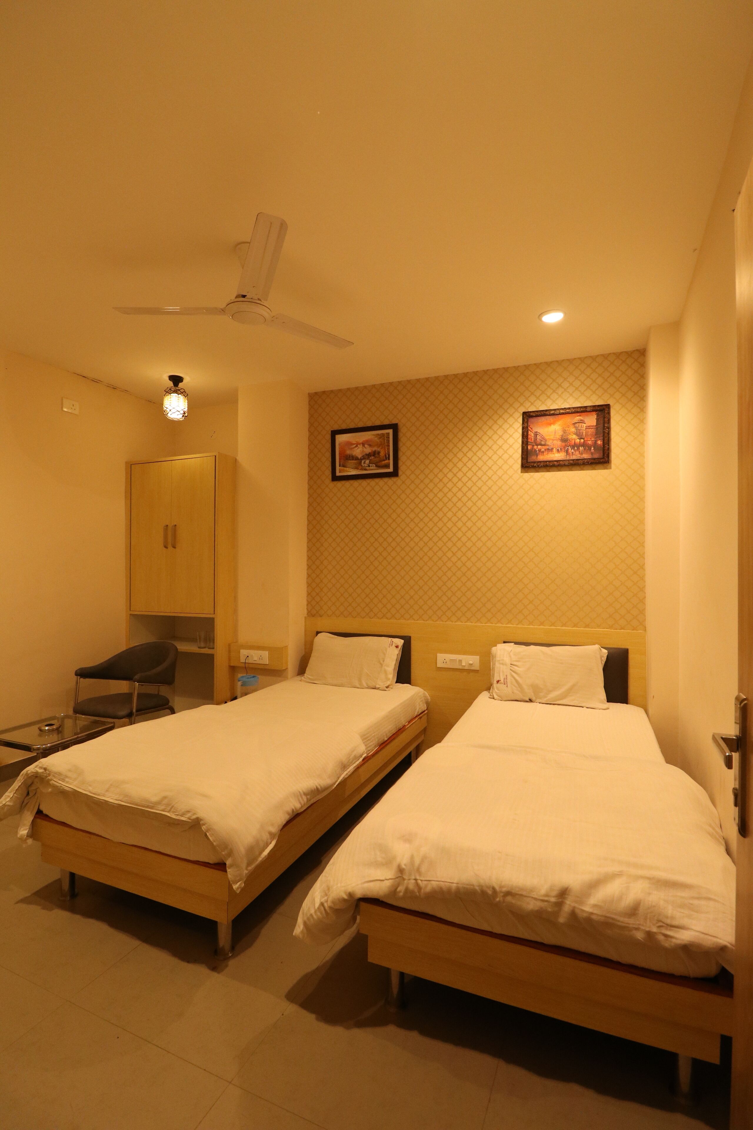 A hotel room with two single beds, a wardrobe, a desk, and a ceiling fan.