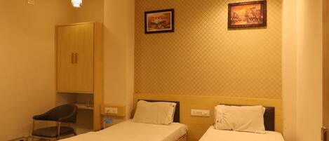 A hotel room with two single beds, a wardrobe, a desk, and a ceiling fan.