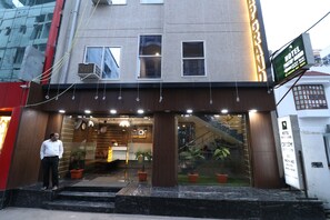 Entrada de hotel con diseño moderno, que incluye una recepción, plantas en macetas y una escalera que conduce al vestíbulo.