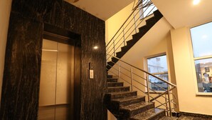 Un ascenseur moderne aux finitions en marbre, un escalier avec des rampes en métal et une grande fenêtre offrant une vue sur l’extérieur.
