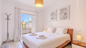 Una habitación de hotel moderna con una cama grande, una mesita de noche con lámpara, un perchero y vistas al exterior.