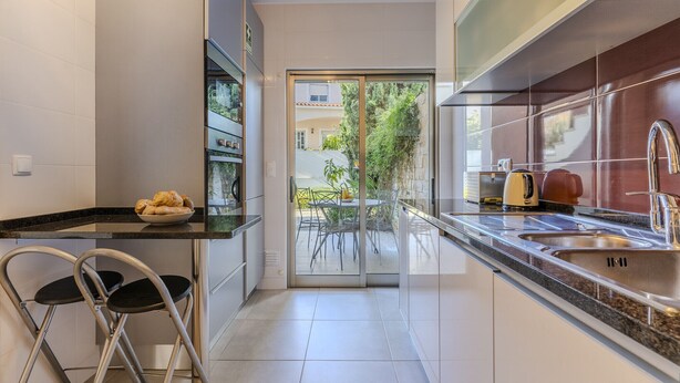 Cocina moderna con puerta de cristal que da a un patio exterior, electrodomésticos de acero inoxidable y un bol de cruasanes en la encimera.