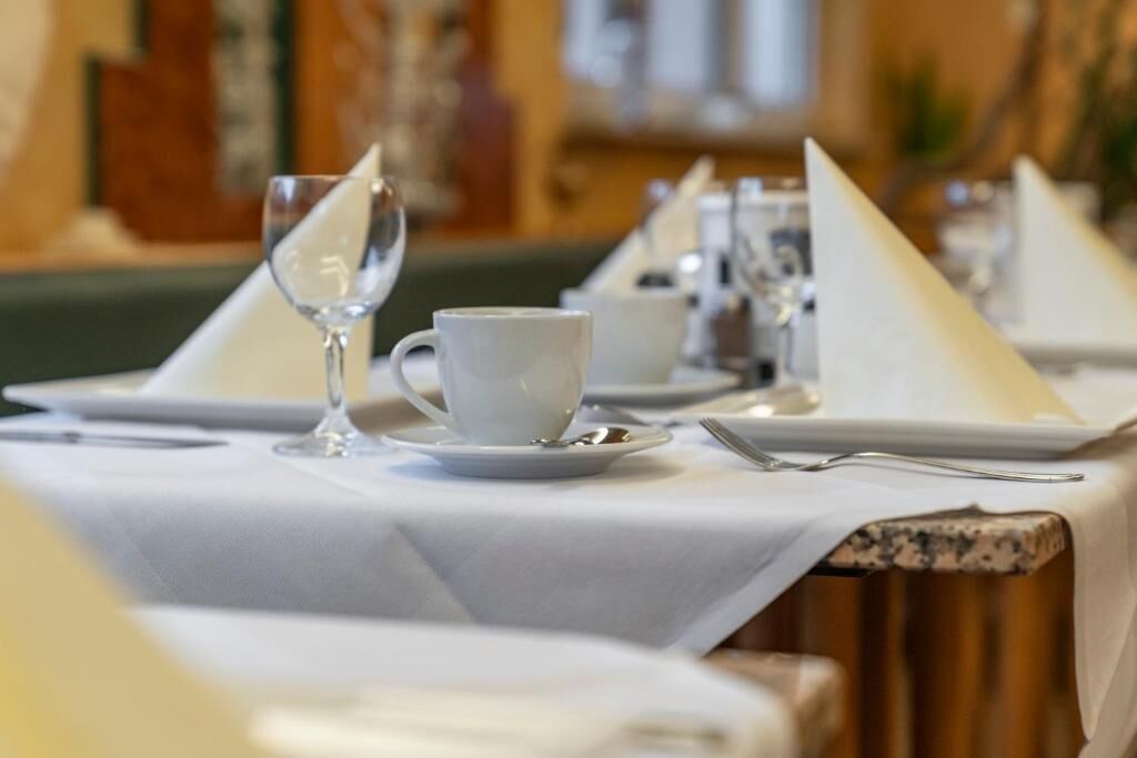 Mesa de comedor con manteles blancos, platos y una copa.
