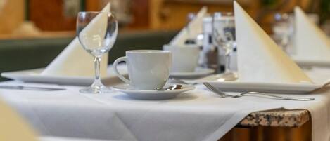 Mesa de comedor con manteles blancos, platos y una copa.