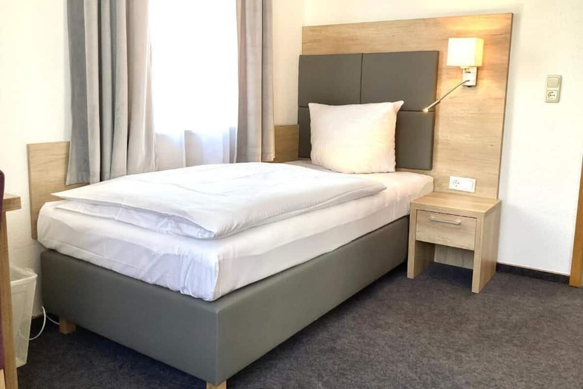 A neatly made bed with a grey headboard, a bedside lamp, and a small wooden nightstand.