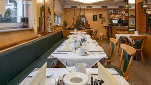 Un restaurant avec une longue table à manger dressée pour le repas, un banc vert rembourré et un coin cuisine en arrière-plan.