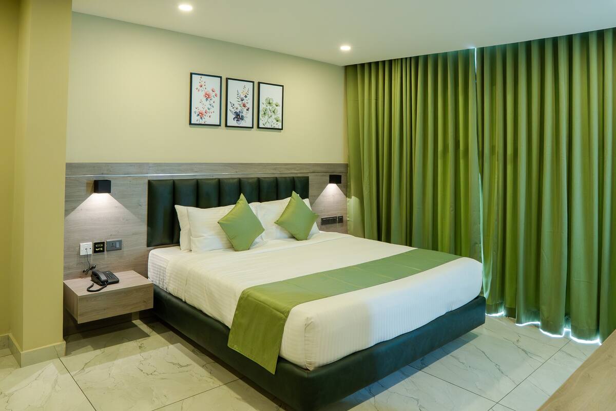 Une chambre d’hôtel avec un grand lit, des rideaux verts et une table de chevet avec un téléphone.